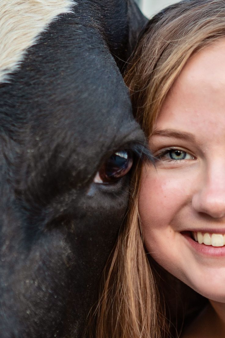 a woman is smiling next to a black and white horse with her face close to the camera