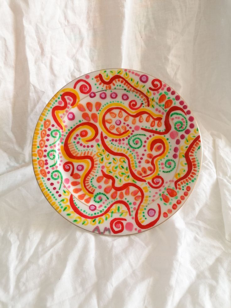 a colorful plate sitting on top of a white cloth covered tablecloth with an intricate design