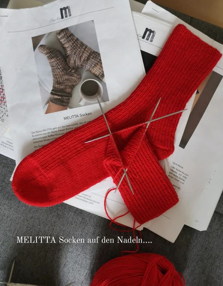 red yarn and knitting needles sit on top of an article of paper with pictures of knitted socks