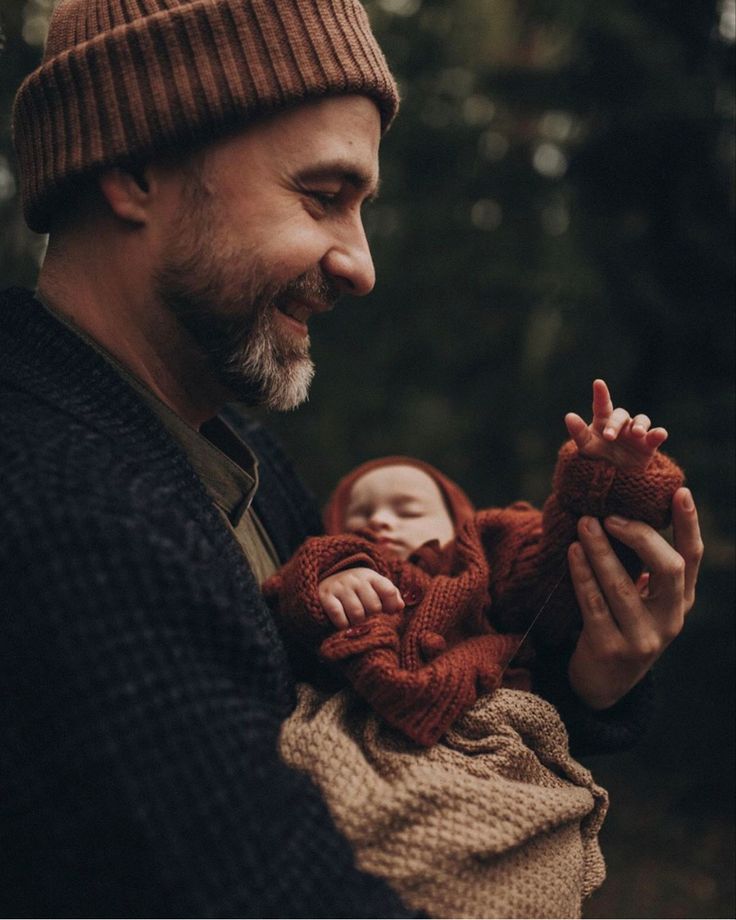 a man holding a baby in his arms and smiling at the camera while wearing a knitted hat