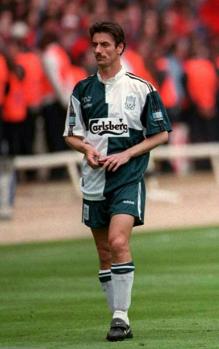 a soccer player walking on the field during a game with fans in the stands behind him