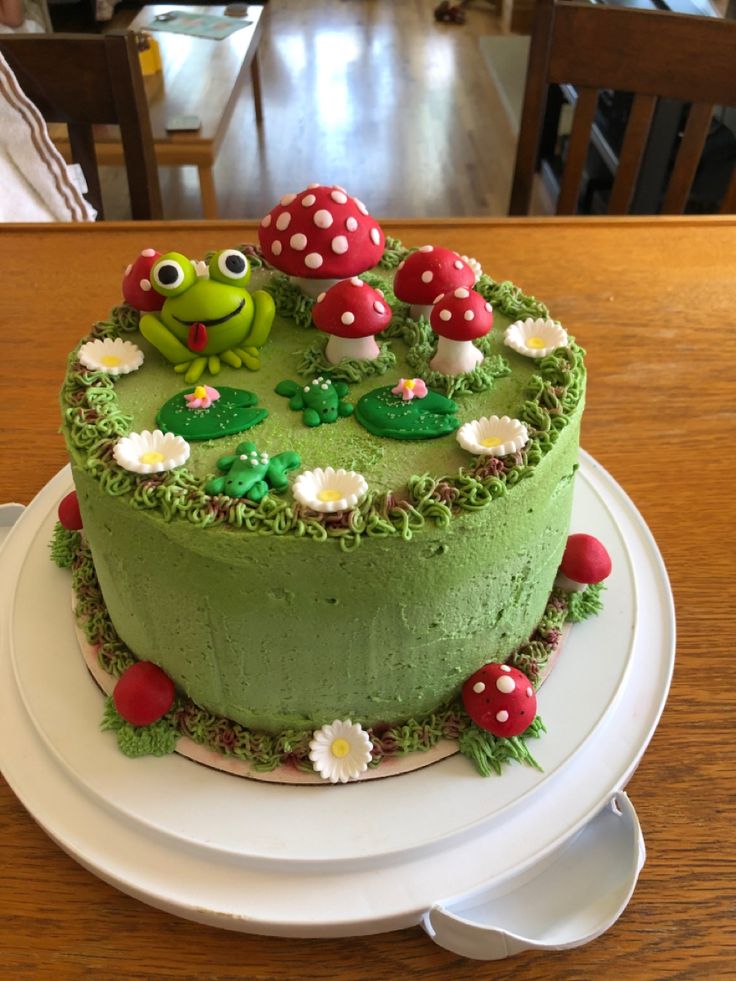 there is a green cake decorated with toades and flowers on the plate next to it