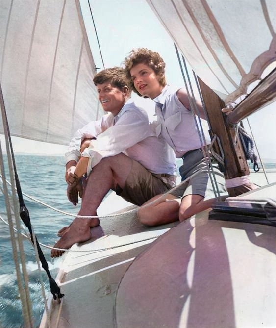 two young men sitting on the back of a sailboat in the ocean, one holding his arm around the other's shoulder