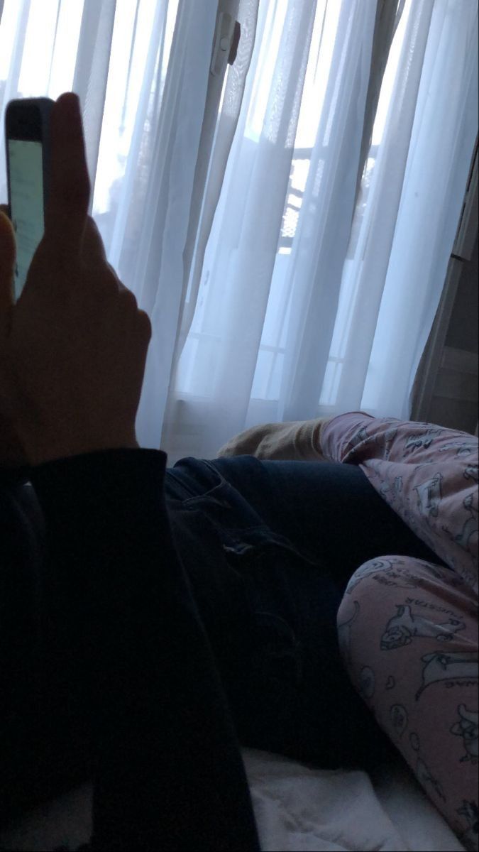 a person sitting on a bed holding a cell phone in their hand and looking at the screen