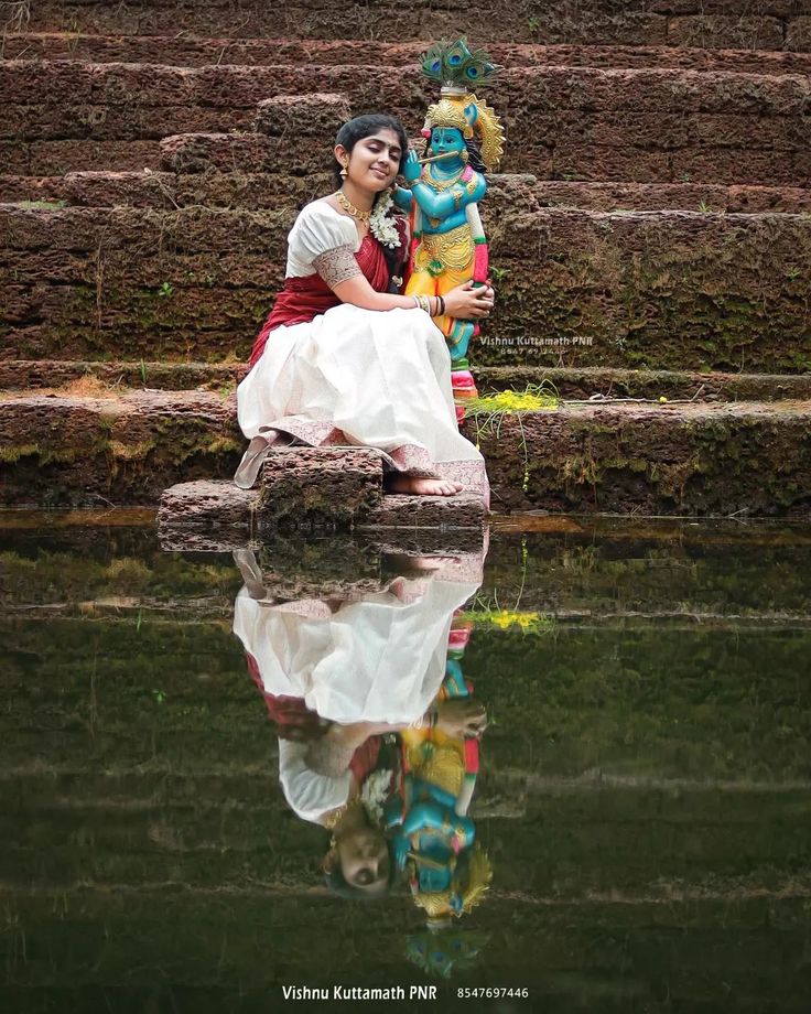 a woman sitting on top of a rock next to a body of water with a statue in the background