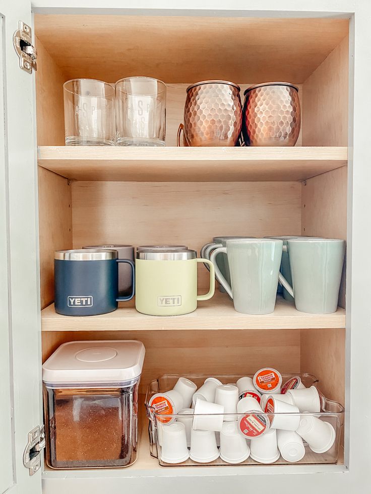 an open cabinet filled with dishes and cups on top of shelves next to containers in front of them