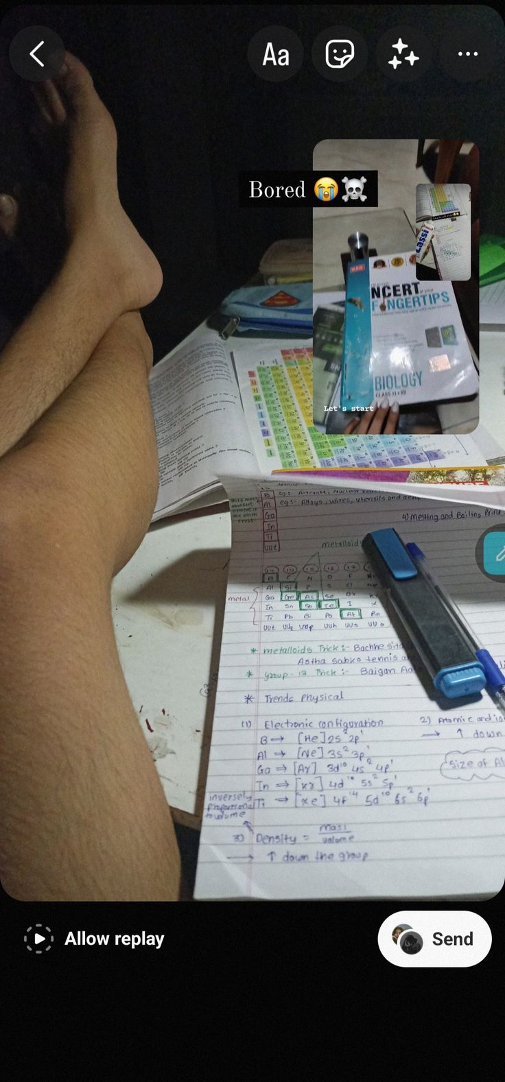 a person sitting at a desk with some papers and pens on top of it, next to a cell phone