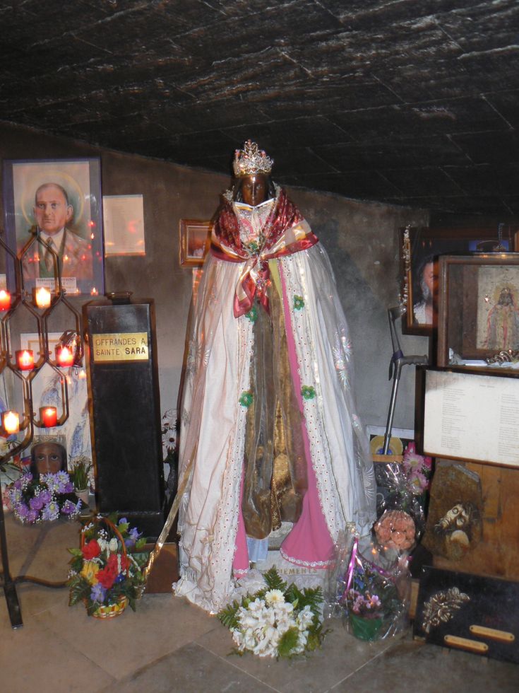 the statue is surrounded by flowers and other items in front of candles, pictures, and paintings