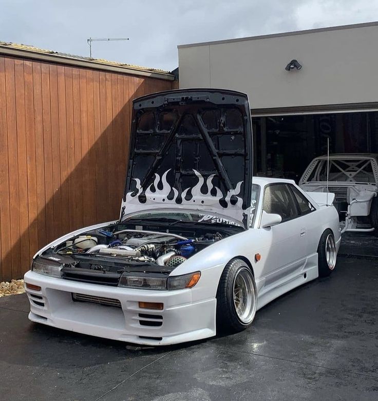 a white car with flames on it's hood parked in front of a garage