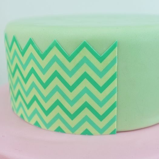 a green and yellow chevron cake on a pink table