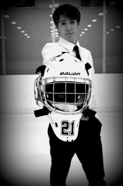 a young man wearing a hockey uniform and holding a goalie's helmet