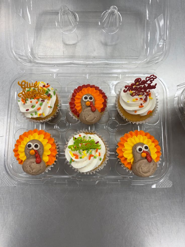 cupcakes decorated like turkeys in a clear plastic container on a silver surface