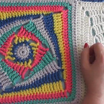 someone is crocheting a square on the floor