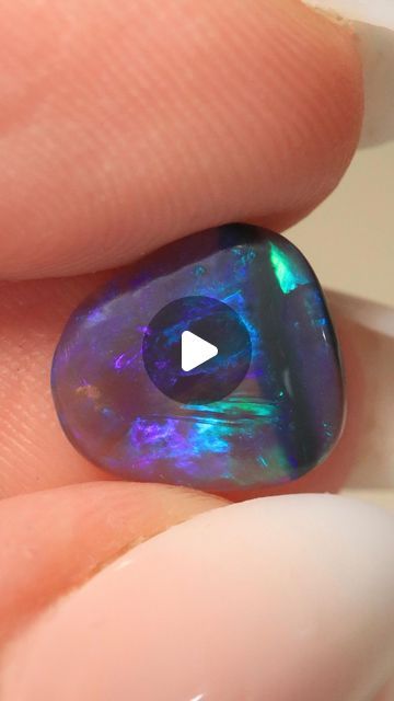 a close up of a person's hand holding a black and blue opal