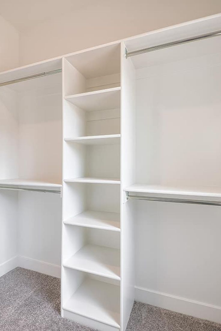 an empty walk in closet with white shelving and carpeted flooring is shown