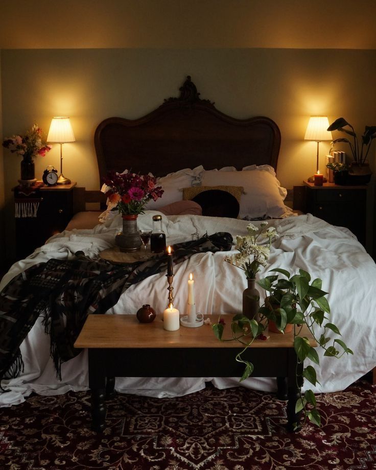 a bed with two candles on top of it next to a coffee table and flowers