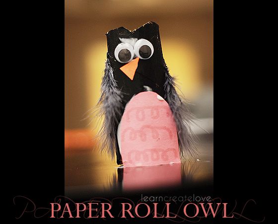 a paper roll owl is holding a pink object with googly eyes on it's face