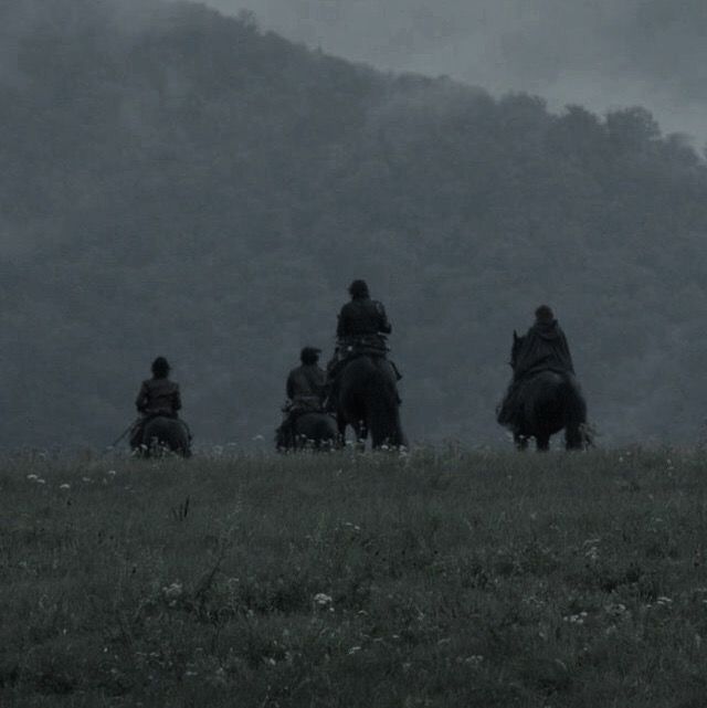 four people riding horses on a hill in the foggy day with mountains in the background