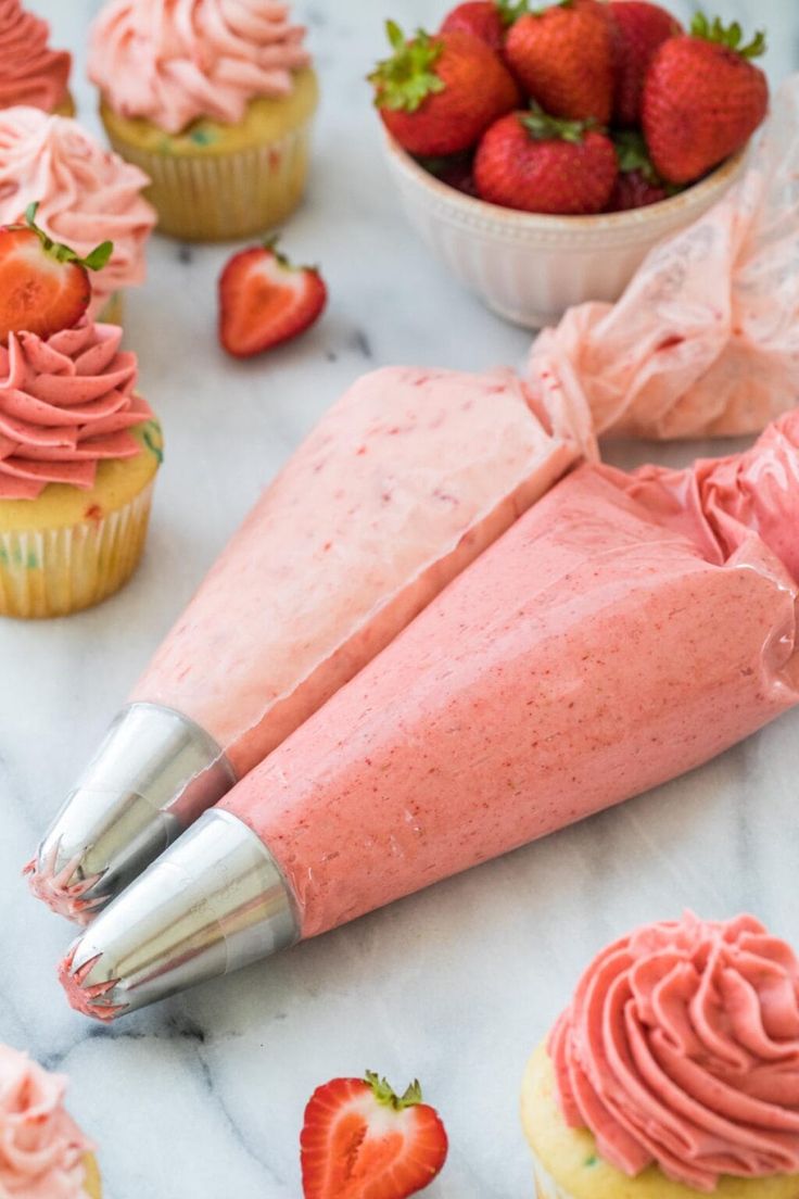 some cupcakes with pink frosting and strawberries in the background on a marble table