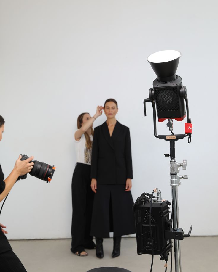 two women are standing in front of a camera and another woman is taking a photo