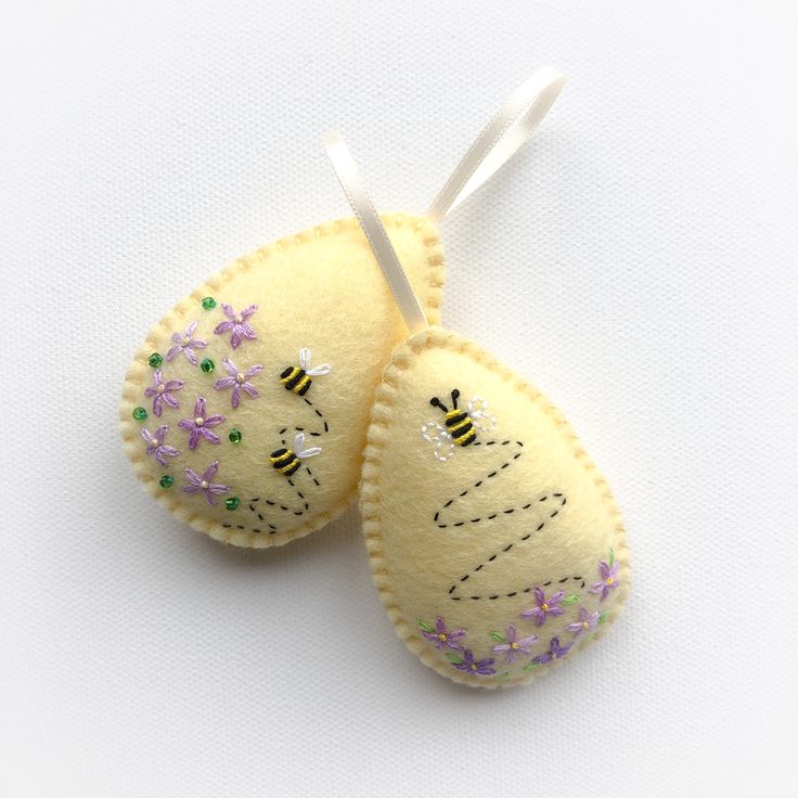 two yellow felt mittens with flowers and bees on them, hanging from a white string