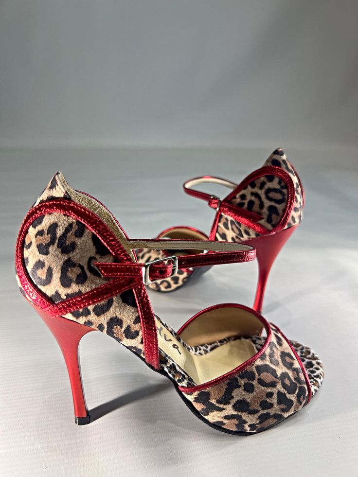 a pair of leopard print high heel shoes with red trimmings and bows on the toes