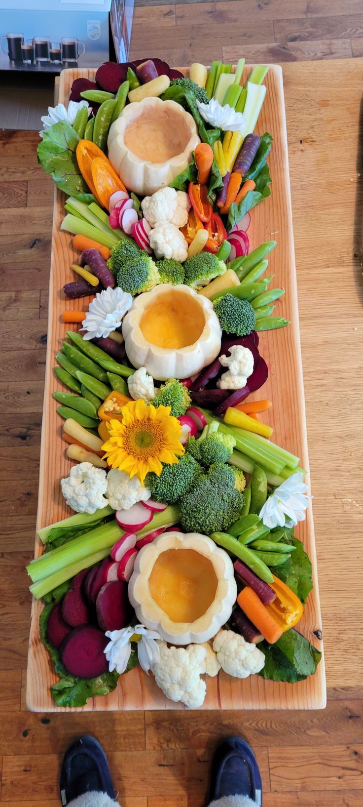 a long wooden tray filled with lots of veggies next to a person's feet