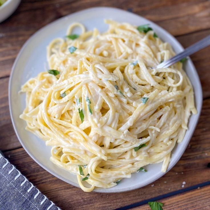 a white plate topped with pasta on top of a wooden table next to a fork