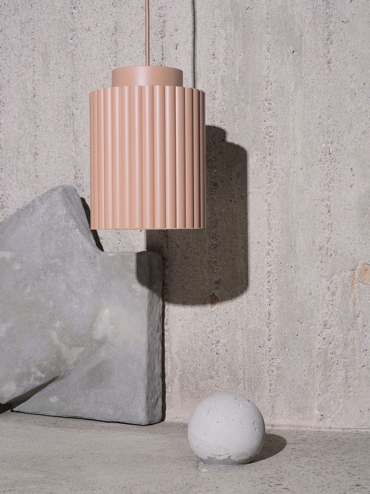 a white ball sitting next to a light on top of a cement block with a pink lamp hanging from it