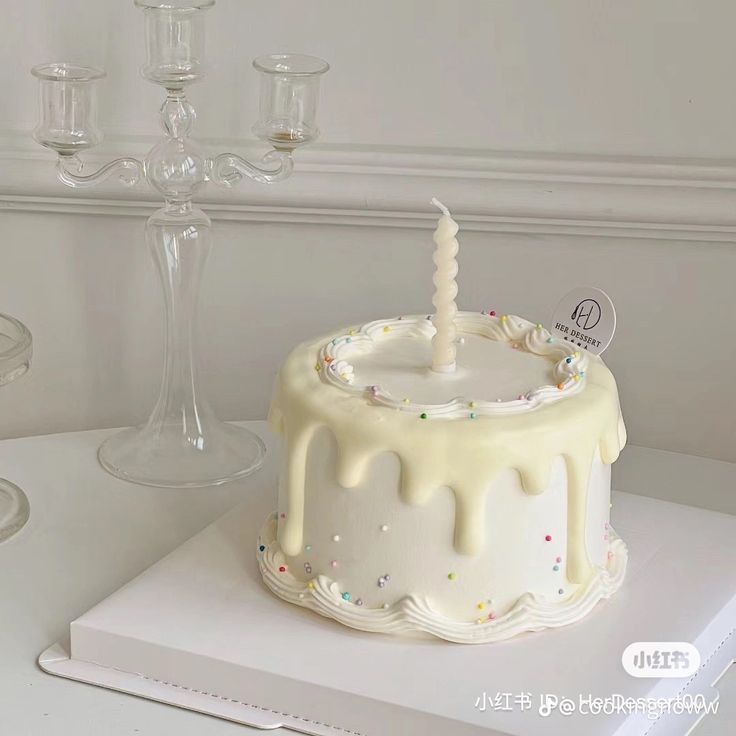 a white cake with a candle on top of it next to wine glasses and candles