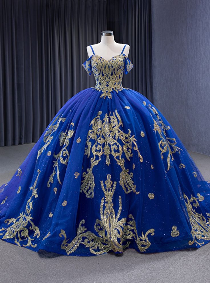 This prom dress, with its intricate gold embellishments, evokes the mystique of a night sky brought to life on fabric. Its corseted bodice, meticulously adorned with sparkling details, sculpts a celestial silhouette. The off-the-shoulder straps add an air of allure, while the expansive skirt unfolds in layers of deep blue tulle, glinting like constellations. Each swirl and step in this gown promises to weave an evening of unforgettable memories, making its wearer the undoubted star of the night. Royal Blue Ball Gown, Royal Blue Quinceanera Dresses, Royal Blue Quinceanera, Quinceanera Dresses Blue, Blue Ball Gowns, Spaghetti Strap Prom Dress, Sequin Prom Dress, Blue Tulle, Evening Dresses For Weddings