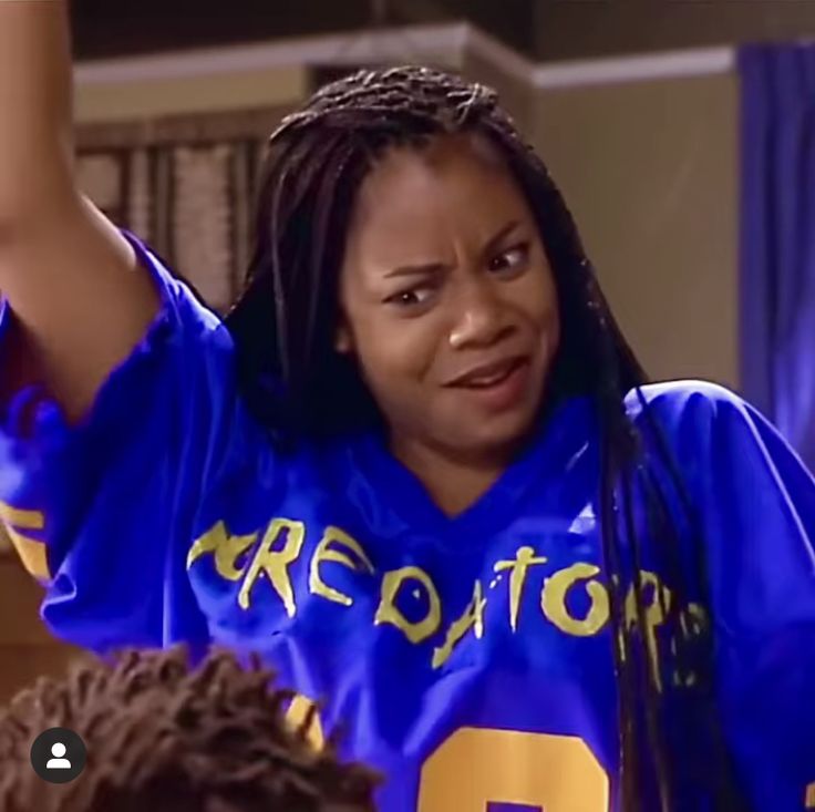 a woman with dreadlocks wearing a blue football uniform and raising her arms in the air