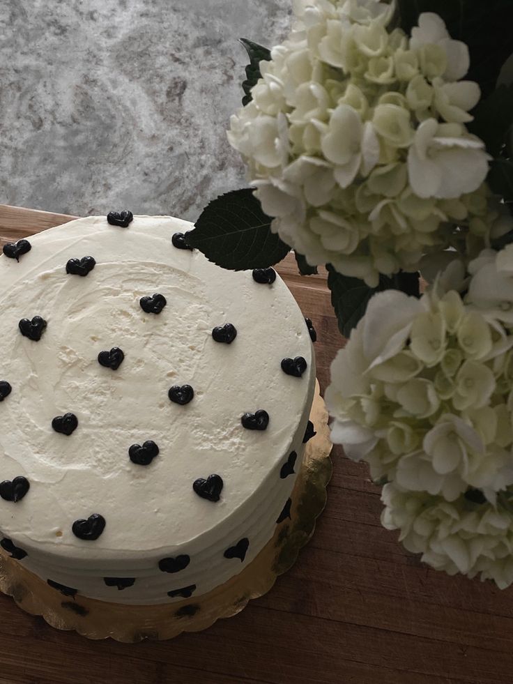 a white cake with black hearts sits on a wooden table next to flowers and water