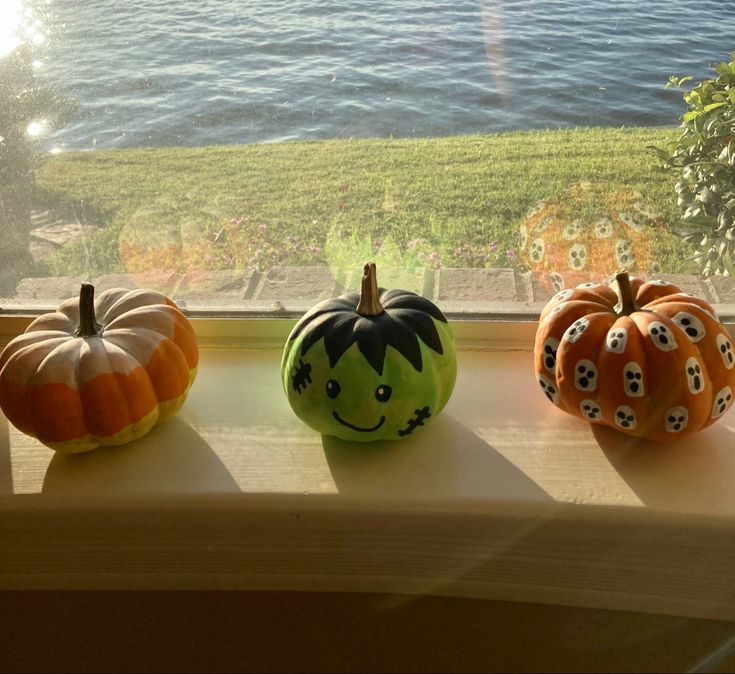 three painted pumpkins sitting on a window sill