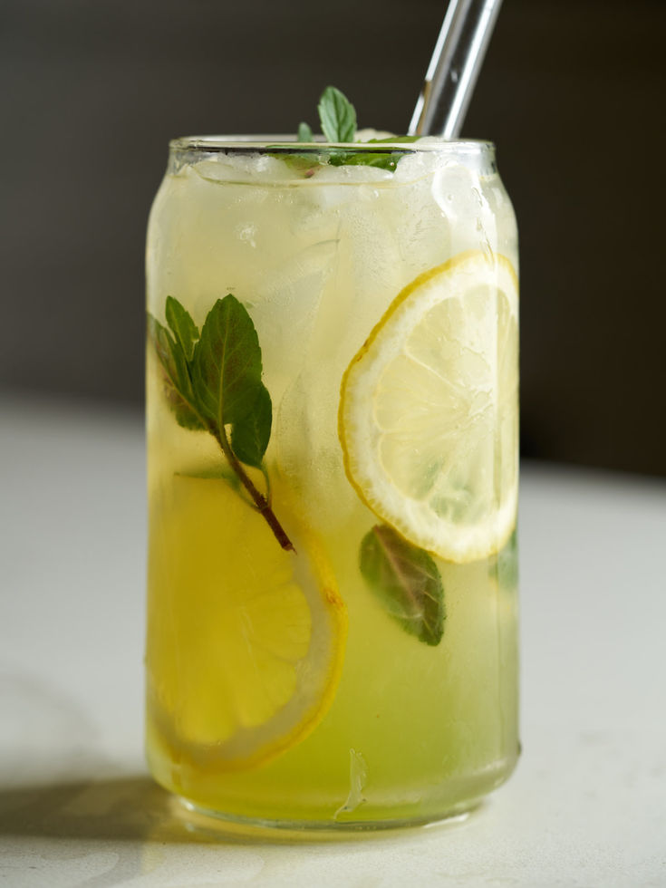 Glass on a counter containing light yellow lemonade, ice and sprigs of mint. Mint Lemonade Aesthetic, Fresh Lemonade Aesthetic, Lemonade Serving Ideas, Asian Lemonade, Can Drink Design, Pretty Lemonade, Lemonade With Mint, Lemonade Aesthetic, Spring Drinks