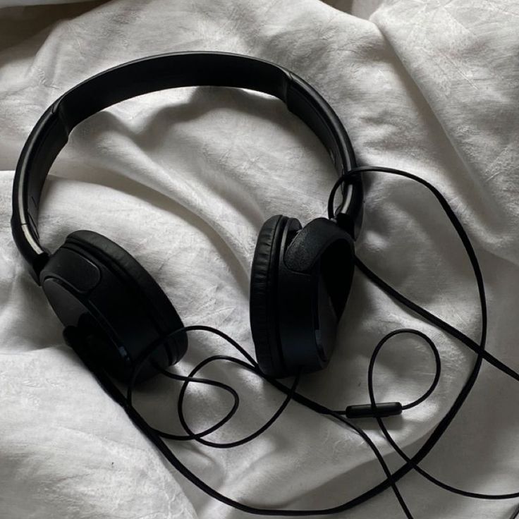 black headphones laying on top of a white sheet covered in sheets and linens