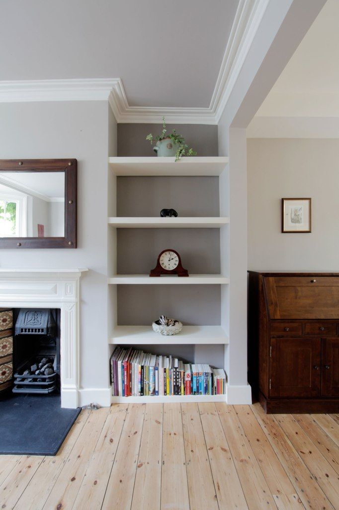 a white book shelf filled with books next to a fire place and clock on top of it