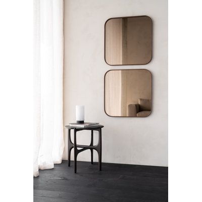 two mirrors on the wall next to a small table with a candle in front of it