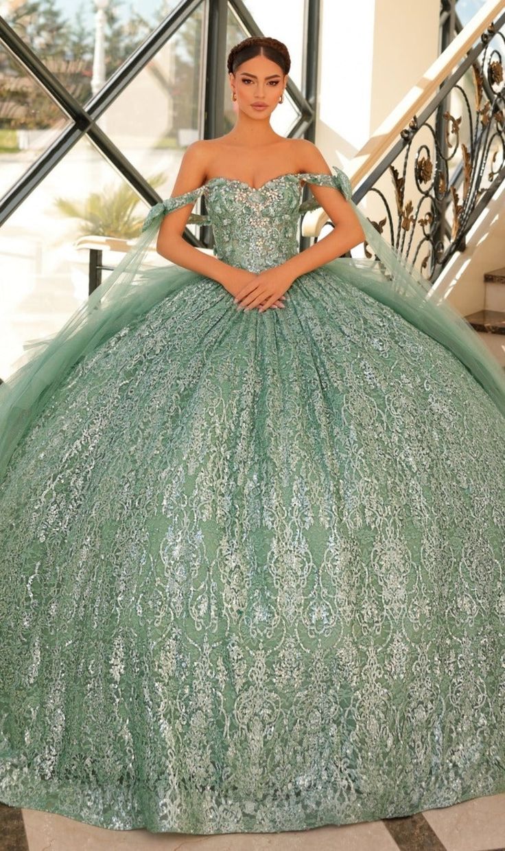 a woman in a green ball gown standing on stairs with her hands on her hips