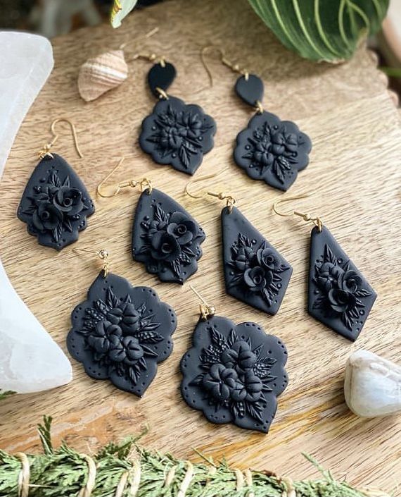 the black earrings are set on top of a wooden table next to shells and plants