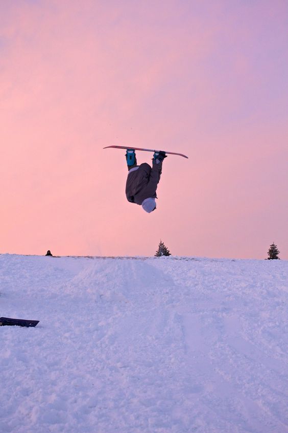 a man flying through the air while riding a snowboard on top of a snow covered slope