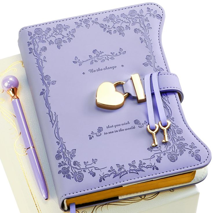 a purple book with a gold heart and key attached to it, sitting next to a pen