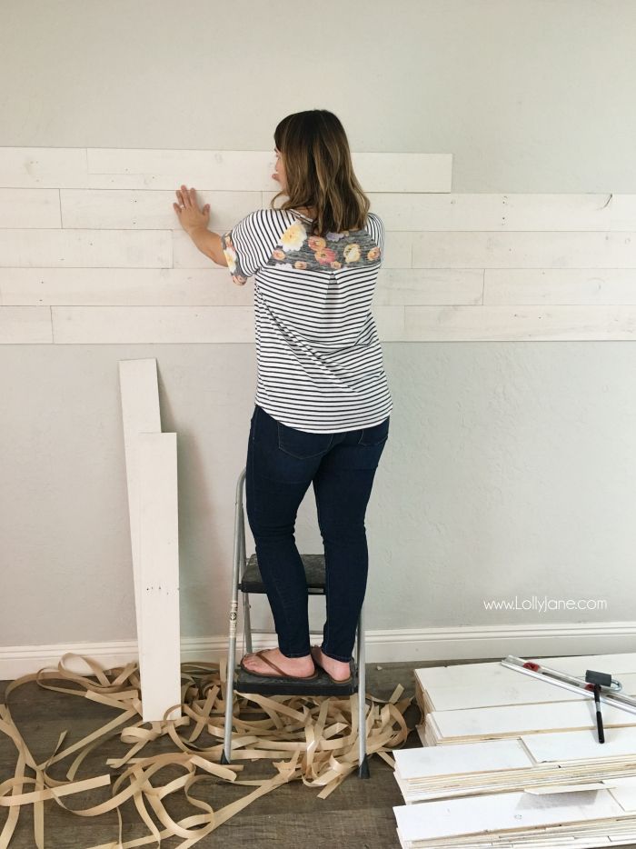 a woman standing on top of a step stool in front of a white board wall