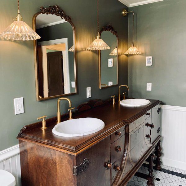 a bathroom with two sinks and mirrors on the wall, along with an antique cabinet