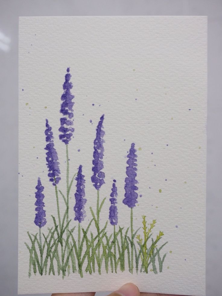 a hand holding up a piece of paper with watercolor paint on it and purple flowers