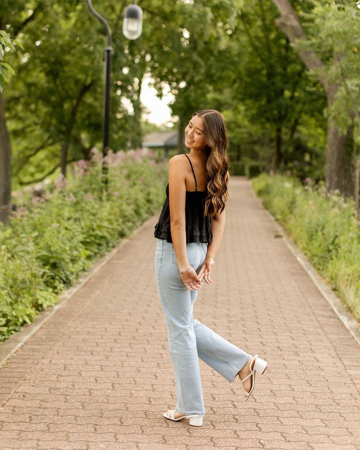 a woman standing on a brick path in front of trees and bushes, looking up at the sky