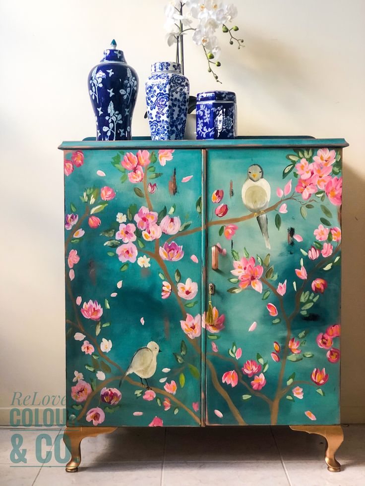 a painted cabinet with vases and flowers on the top, in front of a wall