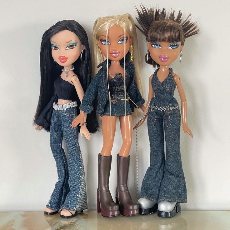 three dolls standing next to each other in front of a white wall and one is wearing jeans