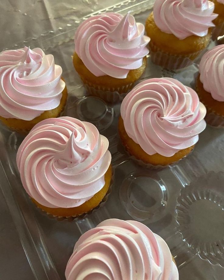 cupcakes with pink frosting sitting on a plastic tray