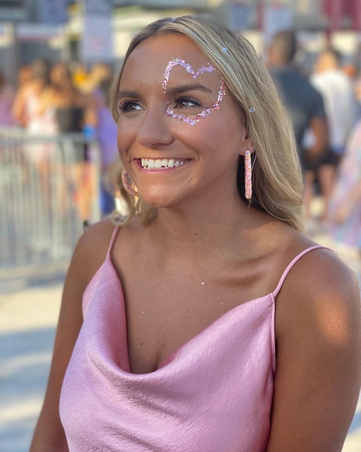 a woman with face paint smiling at the camera while wearing pink dress and earrings on her head